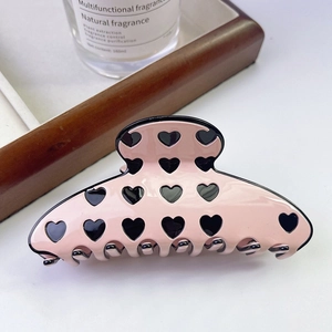 Close-up of a pink acetate hair claw clip featuring black heart patterns on a wooden tray