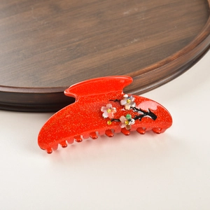 Détail de la pince à cheveux en acétate rouge avec motifs floraux de prunier et strass