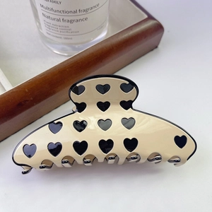 Detailed view of a large beige acetate hair claw clip with black heart patterns on a table