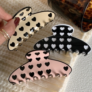 Three acetate hair claws with heart patterns in beige, black, and pink for hair styling