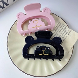 Pinces à cheveux ours chic en acétate rose et noir avec détails dorés sur plat blanc