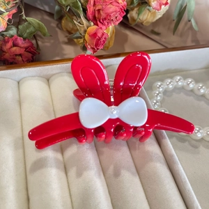 Close-up of a red rabbit ear hair claw clip with a white bow and a pearl detail