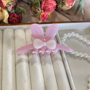 Detailed view of pink rabbit-ear hair claw with white bow and pearl on display