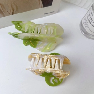 Detail view of acetate pumpkin-shaped hair claws with green and cream marble texture