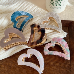 Set of six colorful heart acetate hair claws with gold metal frames on a cozy background
