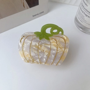 Detailed macro shot of a cream acetate pumpkin hair claw with gold lining and green stem