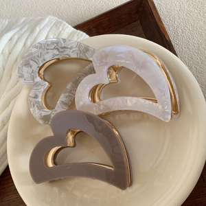 Three acetate heart-shaped hair claws in marble gray, iridescent white, and brown colors
