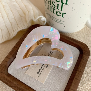 Detail of white acetate heart hair claw clip with golden metal base on a tray