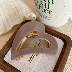 Detailed macro view of heart-shaped hair claw with gold metal frame and pink resin finish