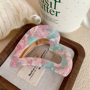 Detail of pink and mint heart-shaped acetate hair claw clip on rustic wooden tray
