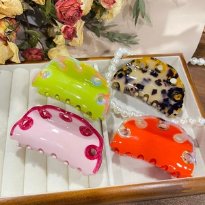 Detailed view of four large colorful acetate hair claws with wavy hollowed design