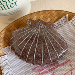 Détail d'une pince à cheveux en forme de coquillage brun foncé avec paillettes et strass