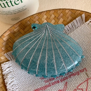 Gros plan sur la pince à cheveux coquillage sarcelle avec lignes argentées et paillettes