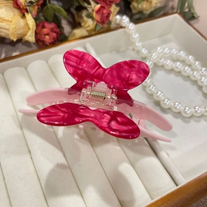Rosa Haarklammer aus Acetat in Schmetterlingsform auf einem luxuriösen weißen Samttablett