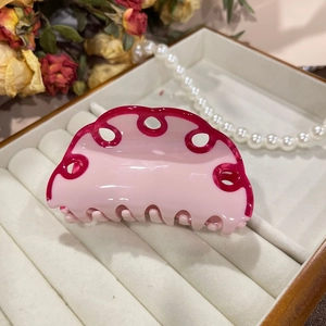 Detailed view of pink acetate hair claw clip with wavy edges and cutout design