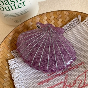 Détail de la pince à cheveux coquillage violette à paillettes sur plateau en bambou