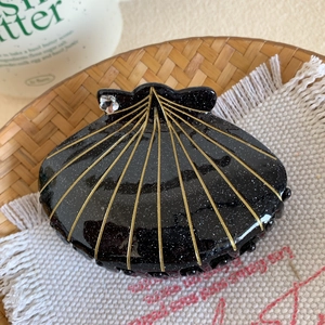 Détail d'une pince à cheveux en forme de coquillage avec paillettes noires et lignes dorées