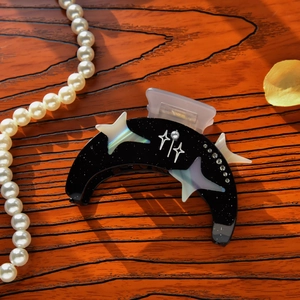 Close-up of crescent moon acetate hair claw with white stars and rhinestones on wood