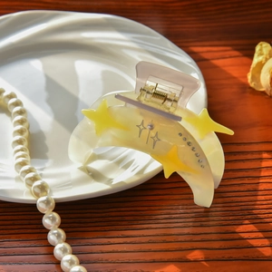 Close-up of cream acetate crescent hair claw with yellow stars and rhinestones on ceramic