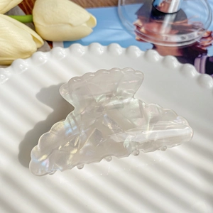 Macro view of shell-shaped pearl hair claw clip with iridescent finish on ceramic tray