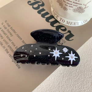 Close-up of black acetate hair claw with white stars, rhinestones and silver glitter details