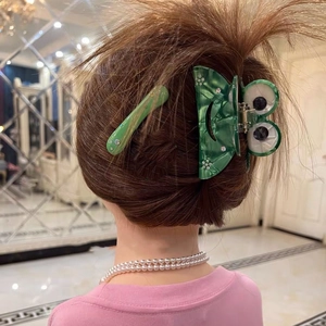 Detail eines grünen Frosch-Haarclips aus Acetat-Set, getragen auf braunem Haar