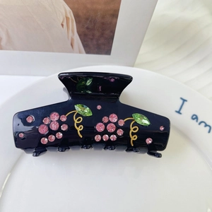 Close-up of black acetate hair claw clip with pink and green rhinestone floral pattern