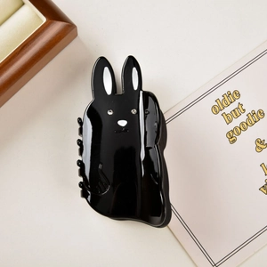 Detailed close-up of a cute black rabbit hair claw clip with crystal eyes on a warm background