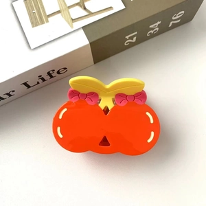 Detail shot of a cute cherry-shaped hair claw clip with orange fruit and pink bows