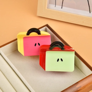 Detail of creative suitcase-shaped hair clips in bright yellow and red acetate finish