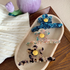 Trois pinces à cheveux fleurs en acétate avec motifs marbre et écaille sur un plateau