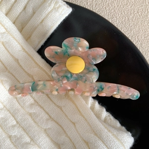 Détail de la pince à cheveux fleur rose à texture marbrée sur un pull en maille