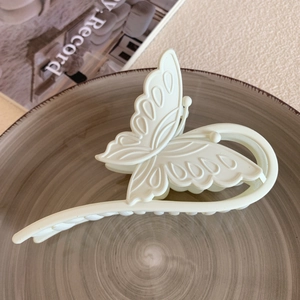 Detailed macro view of a matte cream butterfly hair claw clip on a textured ceramic tray