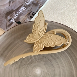 Detail view of a matte khaki butterfly hair claw clip resting on a grey ceramic plate