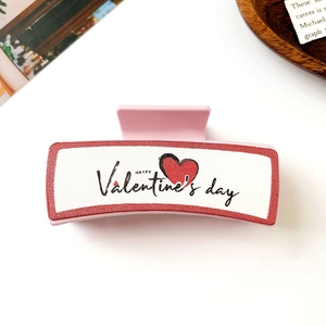 Detail der rosa Herz-Haarklammer mit Valentine's Day Aufdruck auf weißem Grund
