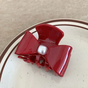 Close-up of a red bow hair claw clip with a glossy finish and white faux pearl detail