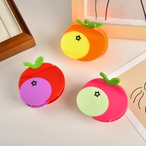 Dettaglio di tre mollette per capelli in acetato a forma di mela in colori arancio e rosso