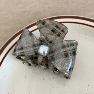Detail view of a dark green bow hair claw clip with a glossy finish and a pearl center