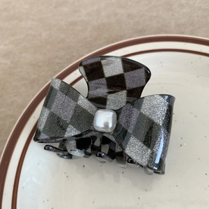 Detail of checkered bow hair claw with central pearl on a ceramic plate decor