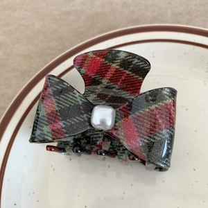 Macro shot of plaid acetate claw clip with a square pearl on a white ceramic plate