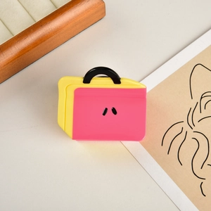 Dettaglio di una pinza per capelli in acetato rosa e giallo a forma di valigetta