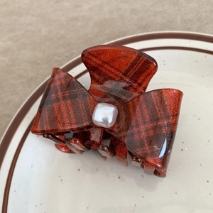 Detail of amber red bow hair claw clip with glitter finish and center pearl accent