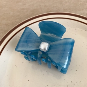 Detailed view of a blue acetate bow hair claw clip with a square faux pearl in a ceramic dish