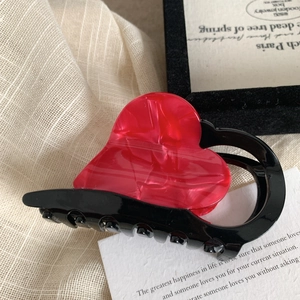 Dettaglio molletta per capelli a cuore rosso marmorizzato con denti neri su tessuto