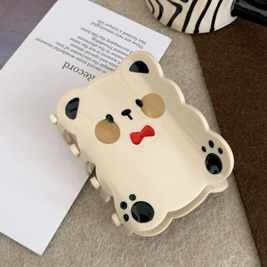 Detail shot of a cute cream bear hair claw clip featuring a 3D red bow and paw patterns