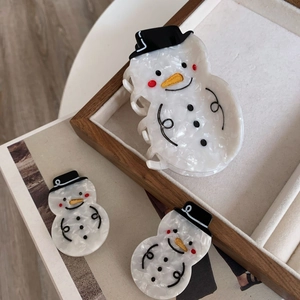 Drei schneemannförmige Haarklammern aus Acetat in Perlweiß auf einem Holztablett