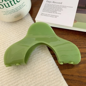 Gros plan d'une pince à cheveux vert herbe en acétate avec un design incurvé lisse