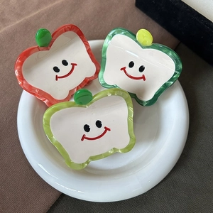 Three cute apple-shaped acetate hair claws with marble texture and smiley faces on white plate