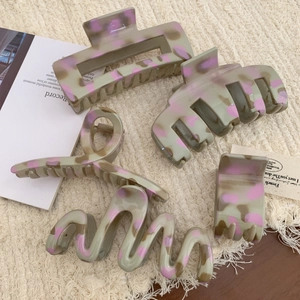 Set of five elegant sage green and purple marble hair claws on a cream knit fabric