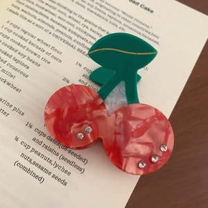 Detailed close-up of cherry hair claw clip made of acetate material on book page